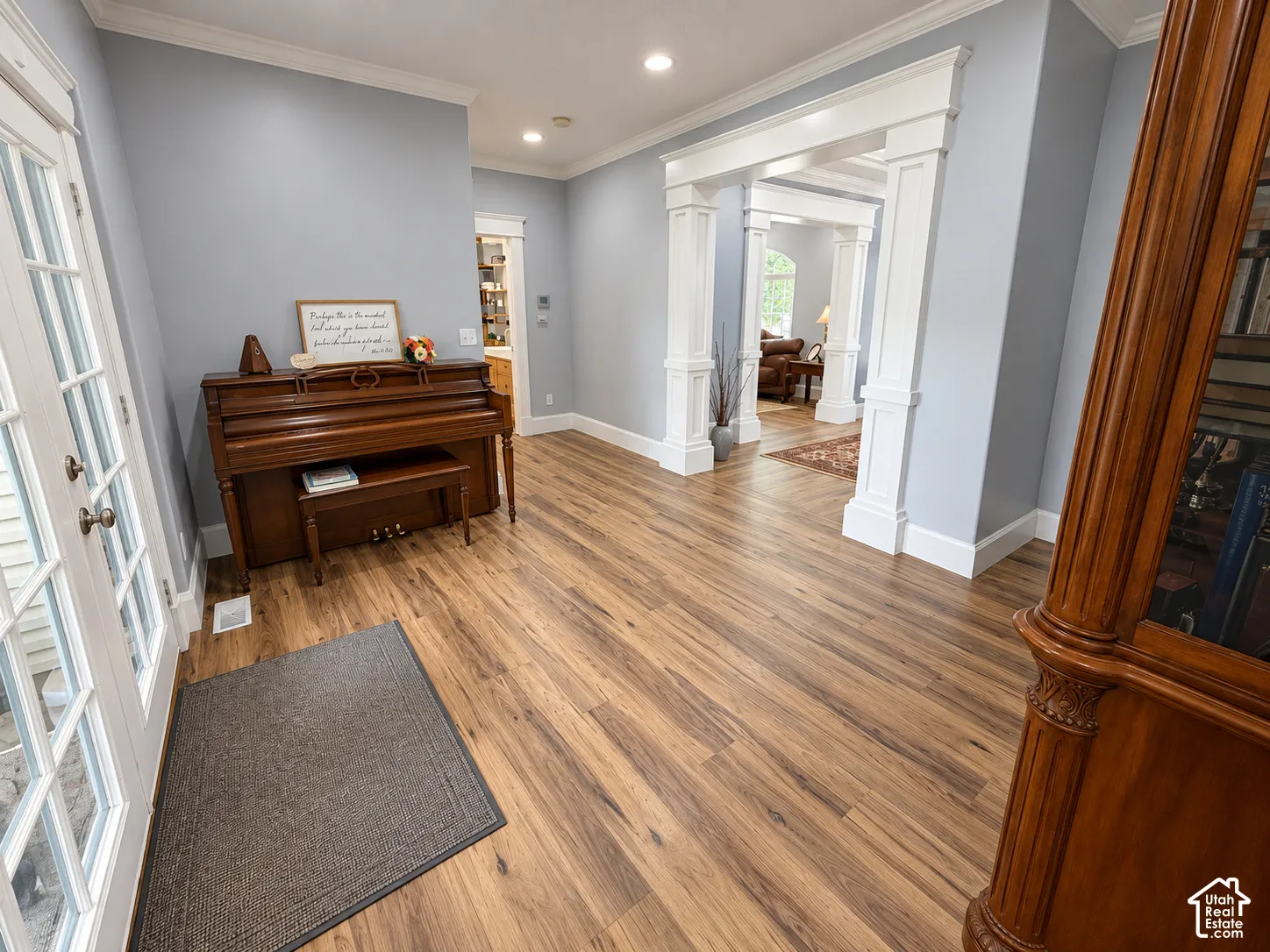 Welcoming foyer showcasing gleaming wood-finish flooring throughout, recessed ceiling lighting, soft blue-gray walls, and architectural columns