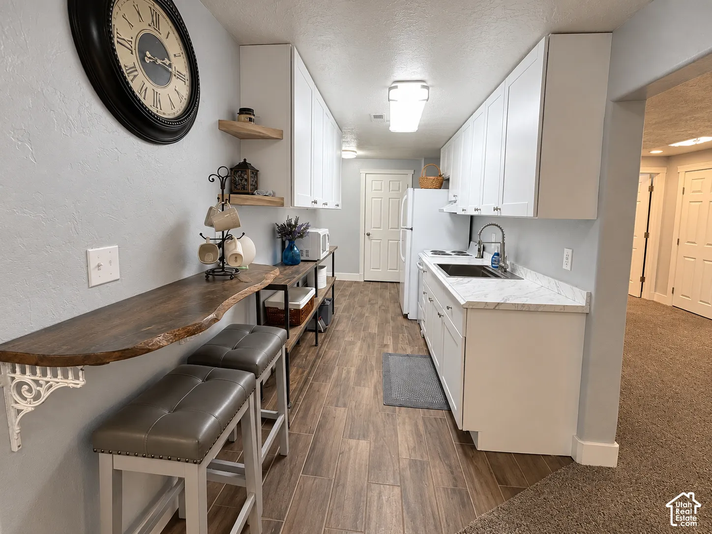Galley-style kitchen featuring wood-finish flooring, white cabinetry, a dark sink with a gooseneck faucet, and light-toned countertops