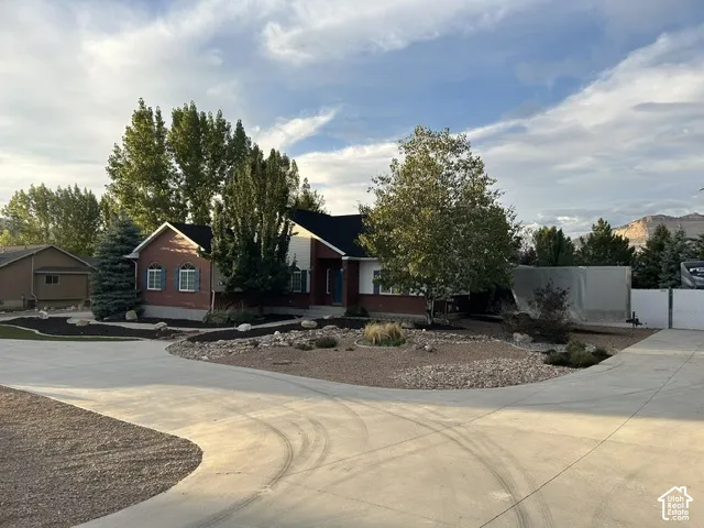 Brick and siding exterior with dark shutters, established landscaping, mature trees, and a spacious concrete driveway