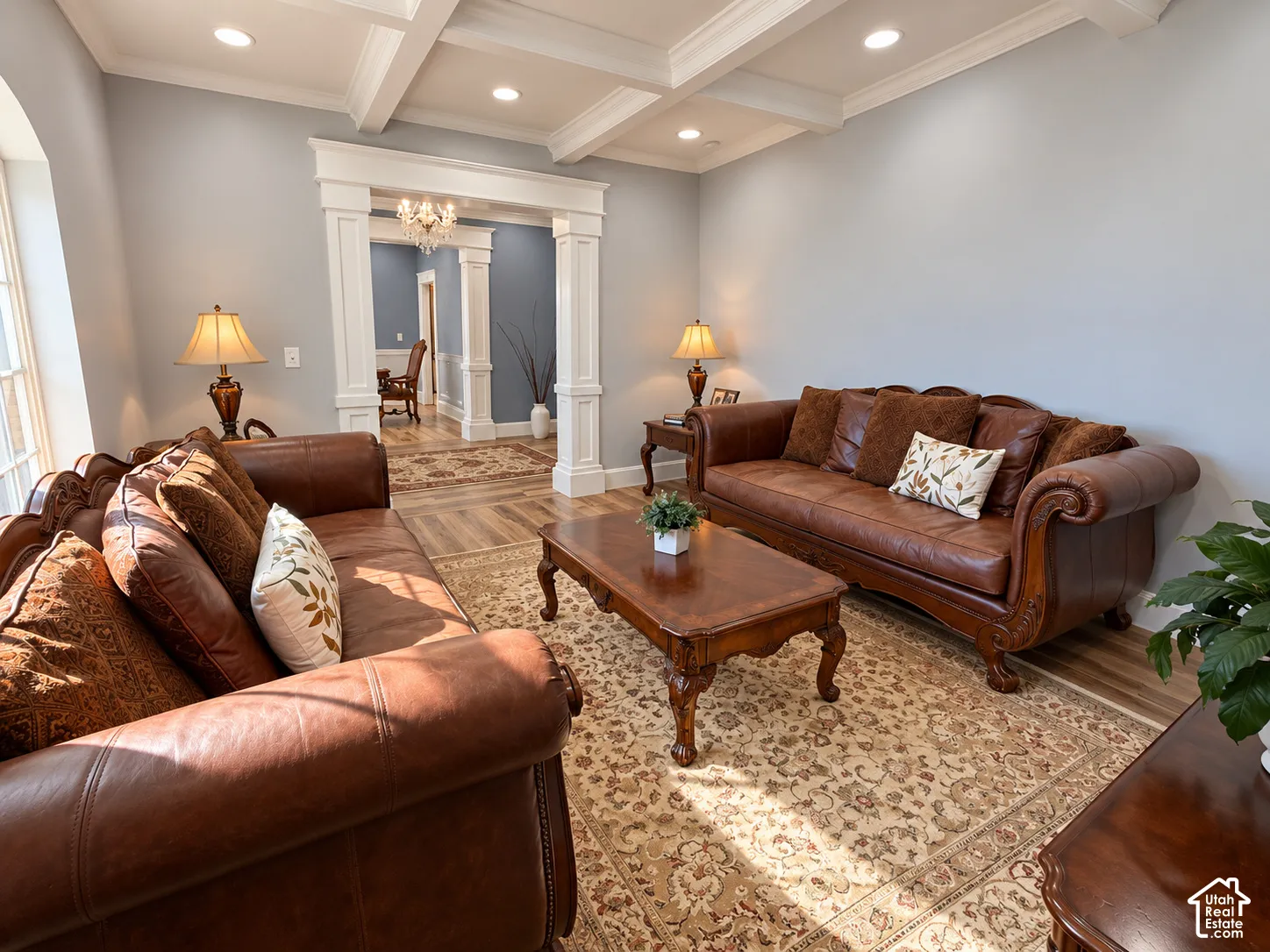 Elegant formal living spaces showcasing rich leather furnishings, coffered ceiling with recessed lighting, and decorative wood-finish flooring throughout