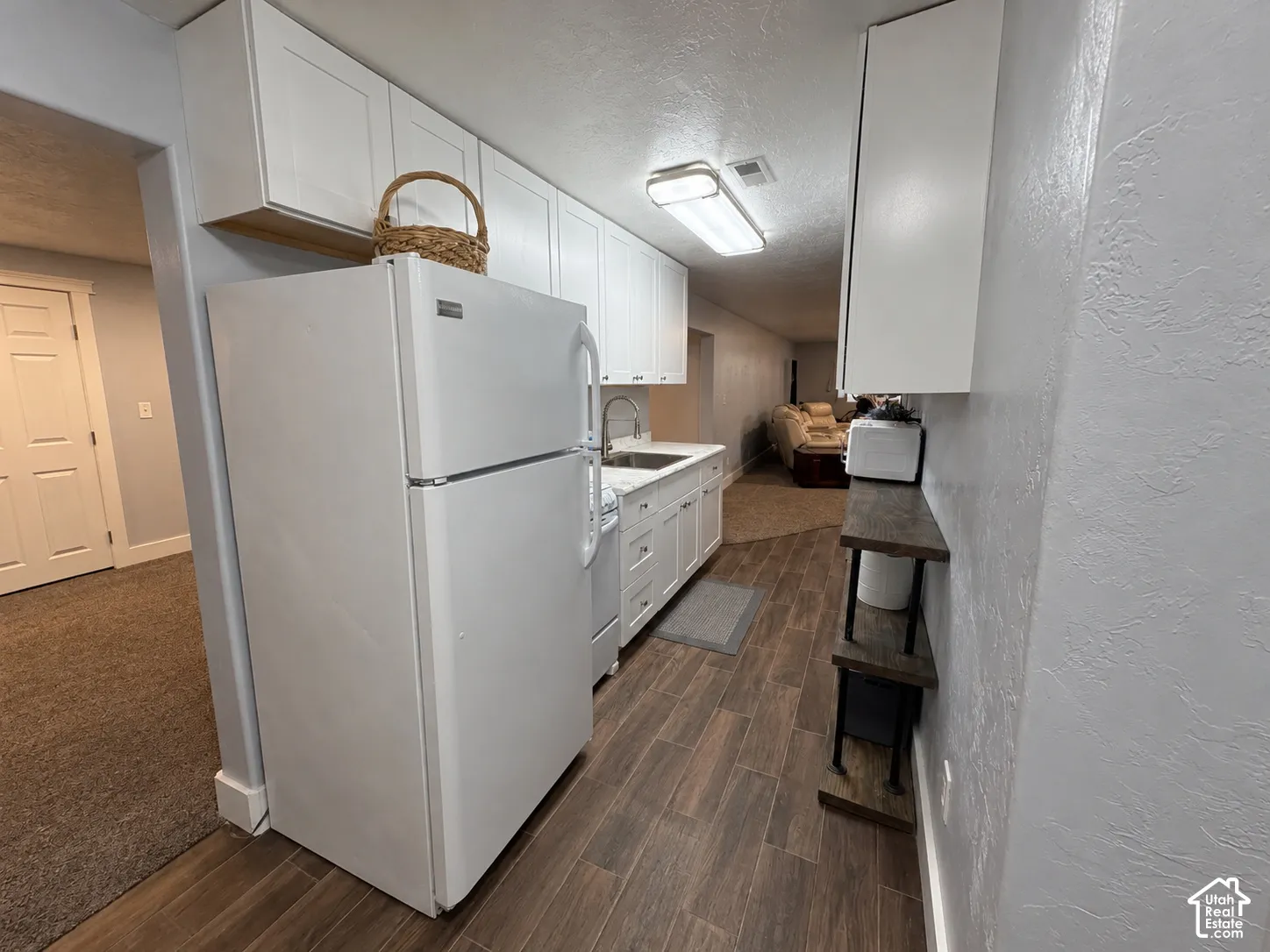 Galley-style kitchen featuring white cabinetry, stainless steel appliances including a refrigerator and electric range, wood-finish flooring, and recessed ceiling lighting