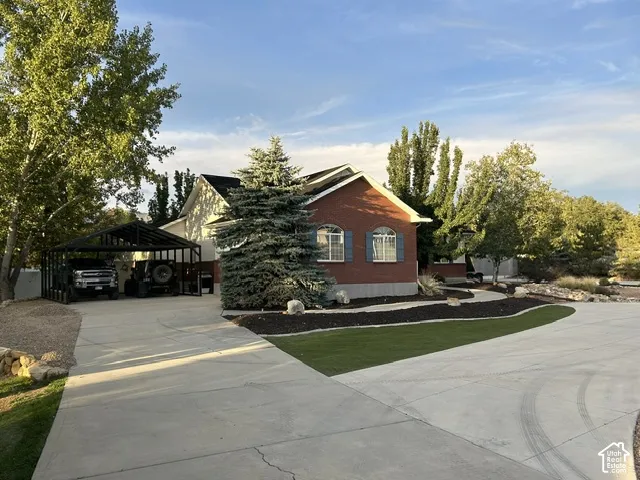 Brick and siding exterior with arched windows, concrete driveway, attached carport, mature evergreen landscaping, and artificial turf accents