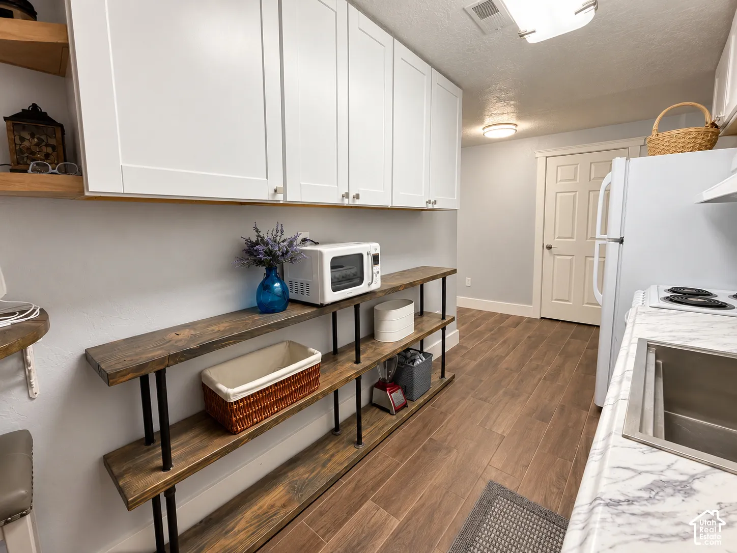 White upper cabinetry, wood-finish flooring, light grey walls, open shelving with wood-finish planks, and a stainless steel sink