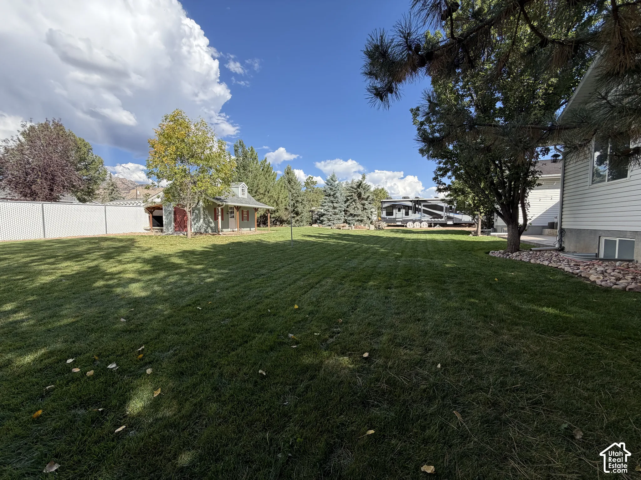 Expansive grassy backyard featuring a detached shed with a covered porch, mature trees, and a privacy fence
