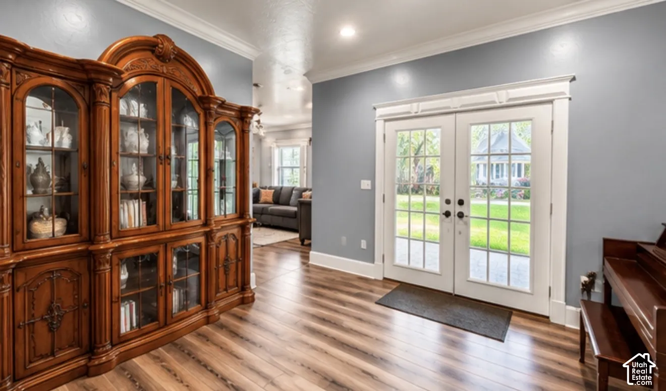 Wood-finish flooring, white crown molding, recessed lighting, and white French doors with exterior access