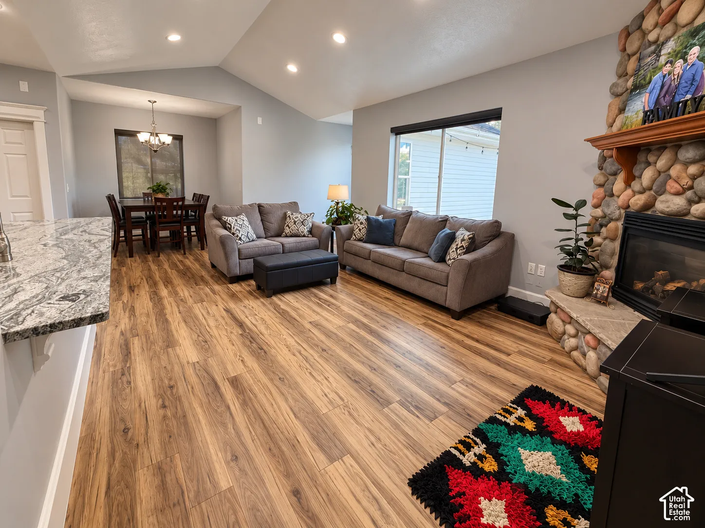 Wood-finish flooring throughout, vaulted ceilings, recessed lighting, stone fireplace, and a granite countertop