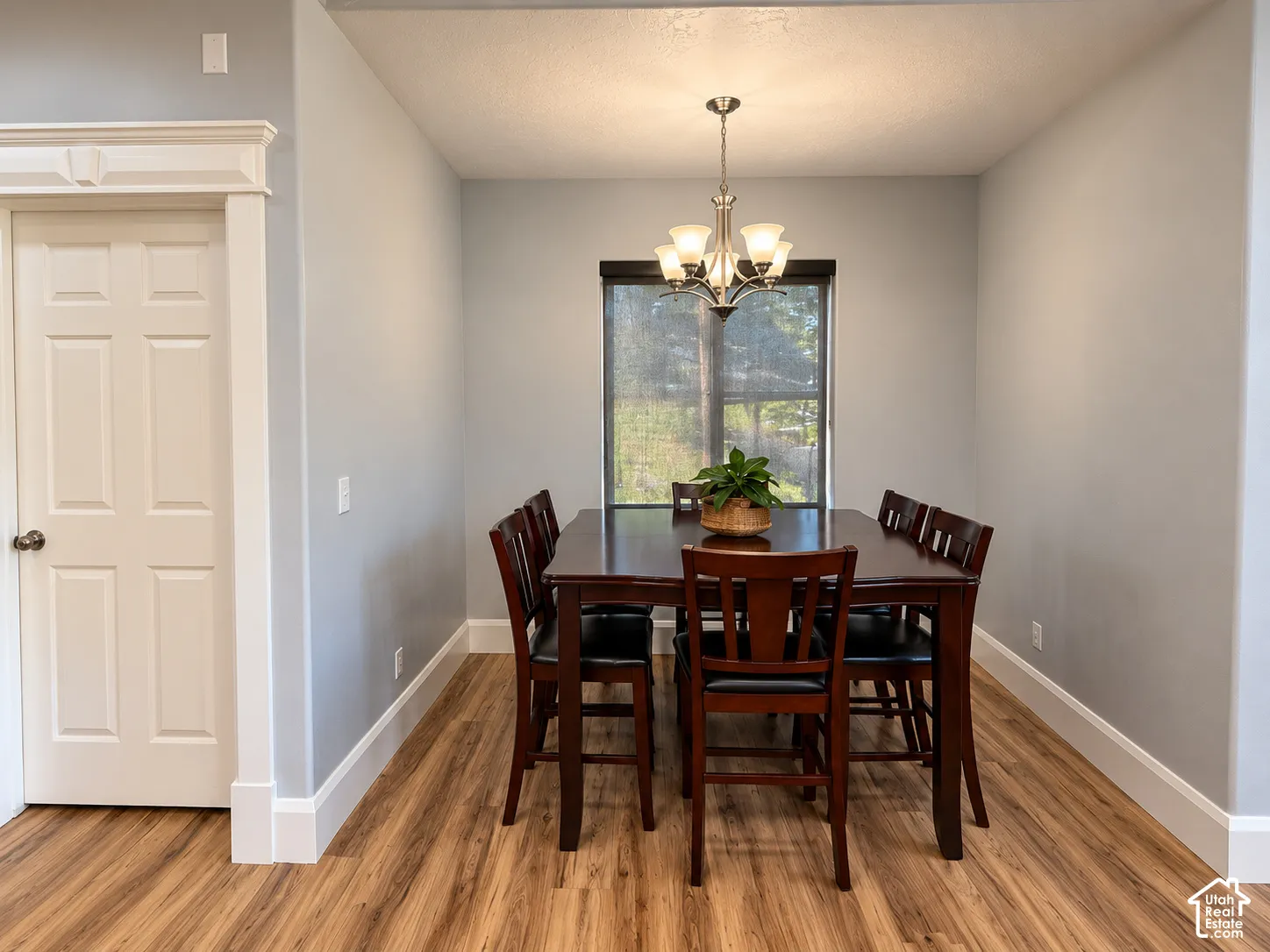Dining area featuring wood-finish flooring, a contemporary chandelier, and a window with a roller shade