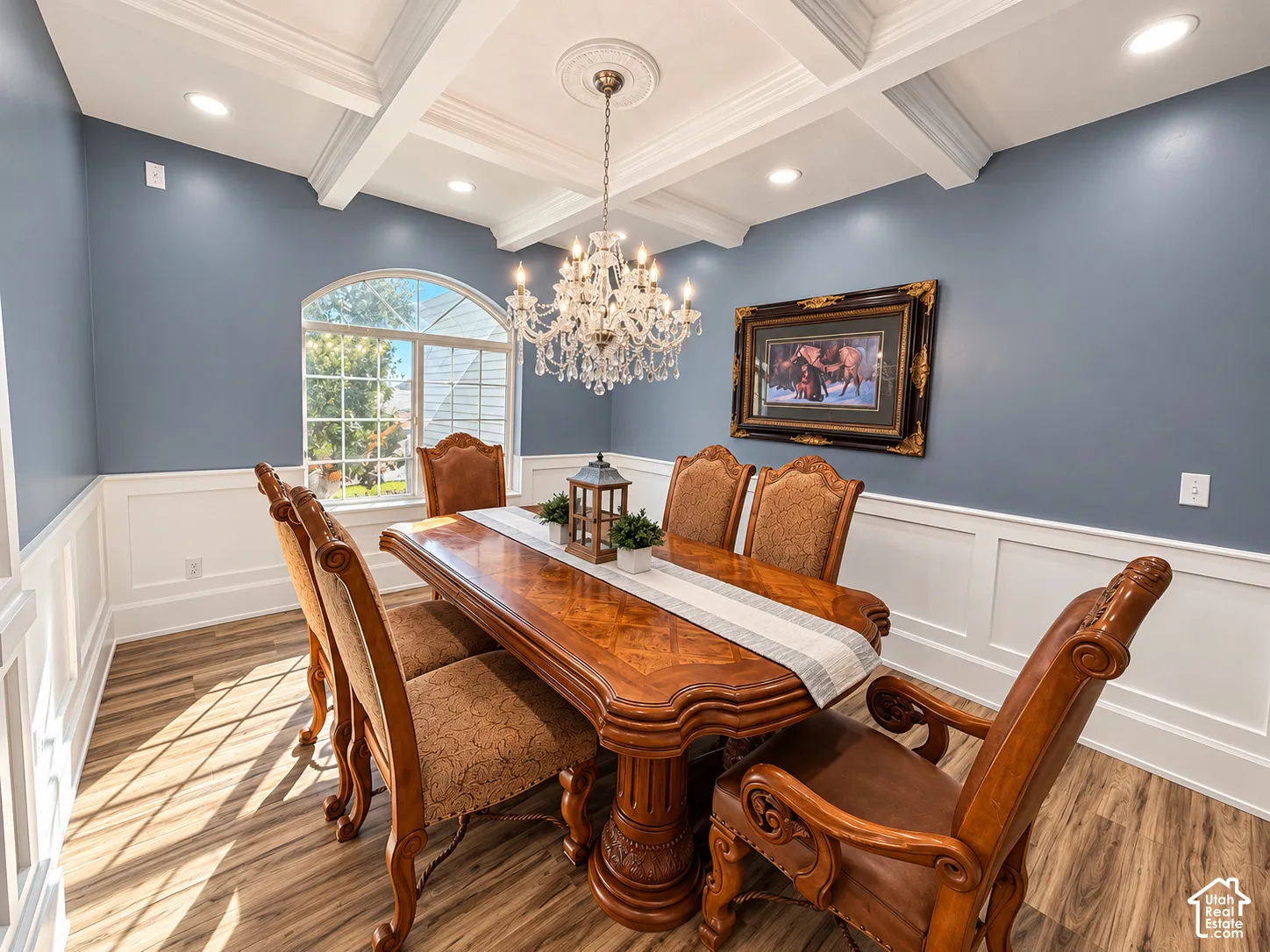 Coffered ceiling with recessed lighting and a crystal chandelier, arched window, wood-finish flooring, and wainscoting