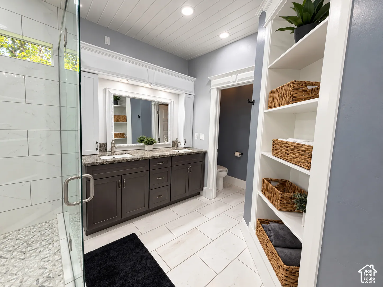 Spa-inspired primary bathroom featuring a dark wood double-vanity with multiple storage drawers, large framed mirror, and ceramic tile flooring