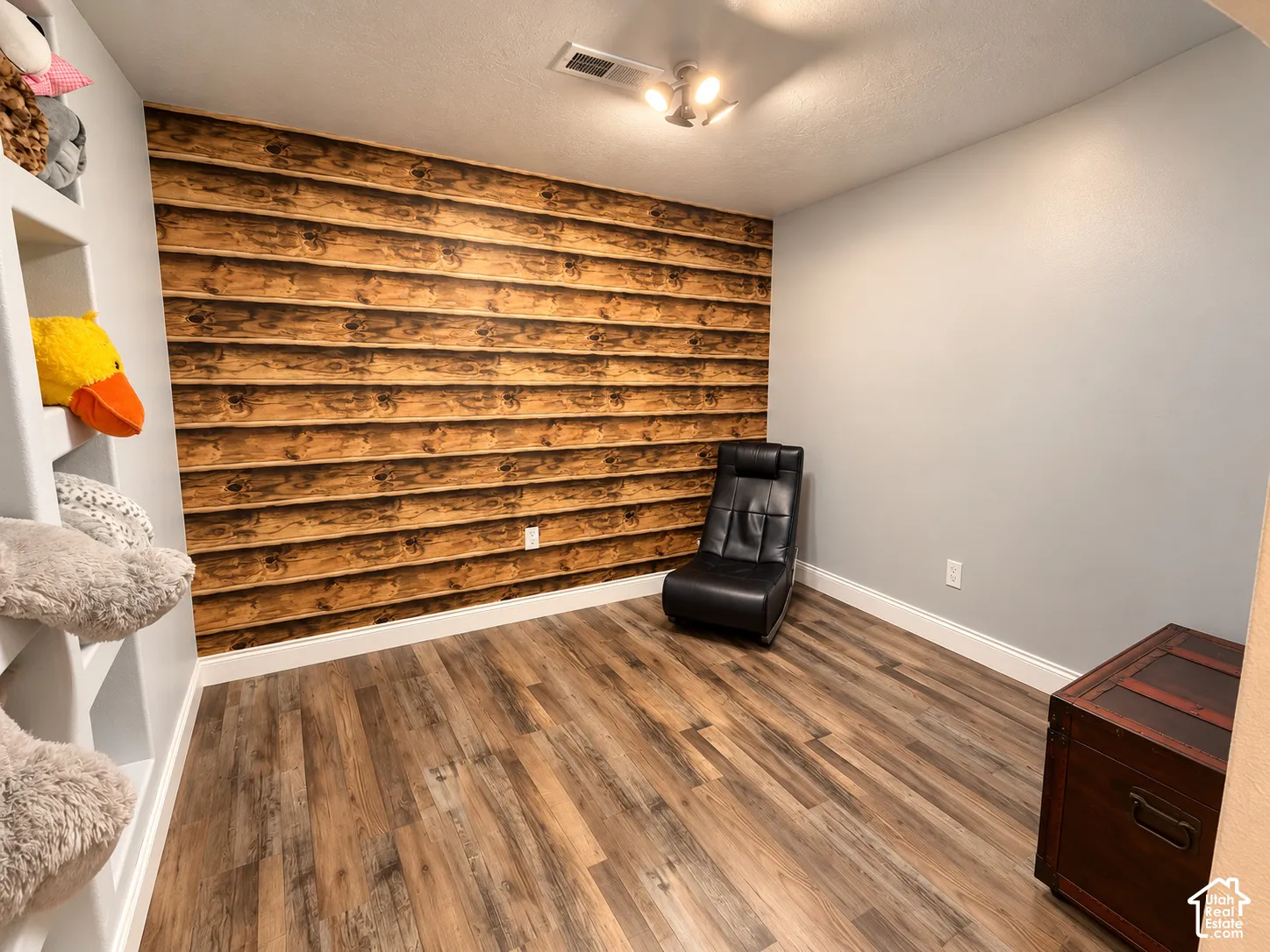 Versatile room featuring warm wood-finish plank flooring, a shiplap accent wall with rich honey tones, white drywall, recessed ceiling lighting, and a dark wood dresser