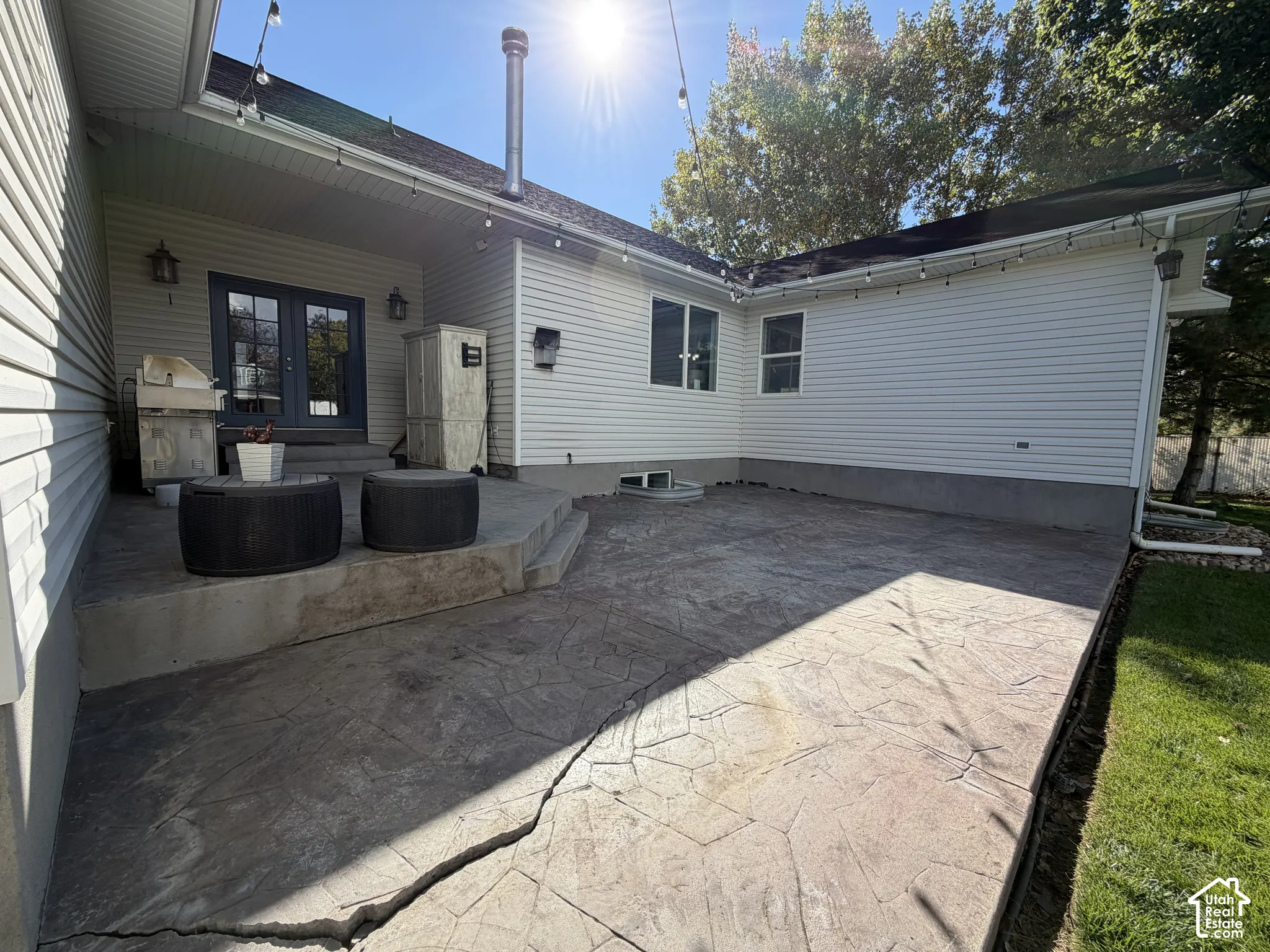 Expansive stamped concrete patio with mature tree backdrop and direct access to the home's rear entrance