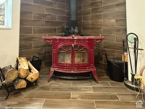 Corner wood-burning stove with a red finish, set against a tile-clad wall, featuring coordinating wood-look tile flooring