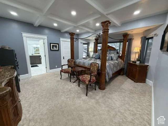 Coffered ceiling, light-toned carpeting, ample window openings, and an open doorway to a bathroom with a vanity