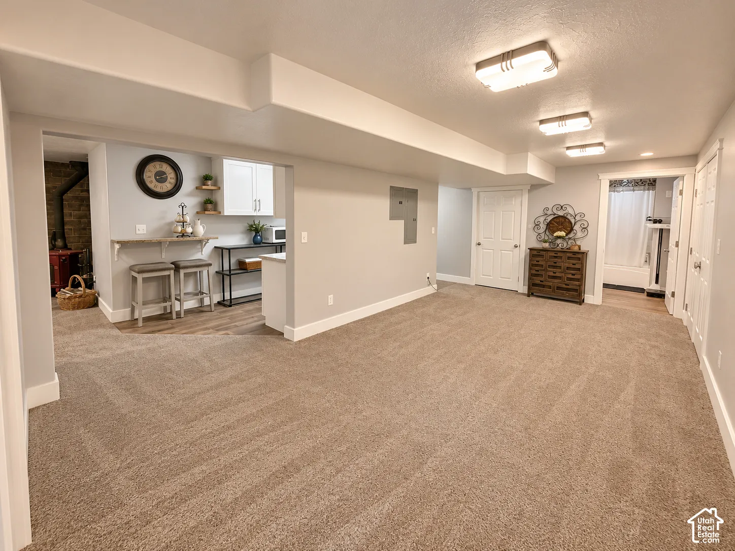 Expansive carpeted area with recessed lighting, complemented by a compact kitchen featuring white cabinetry and wood-finish flooring