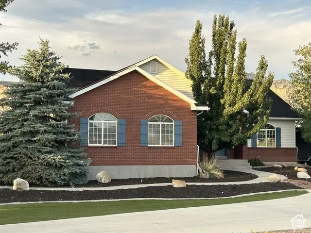 Brick and siding exterior with arched windows, blue shutters, and mature landscaping