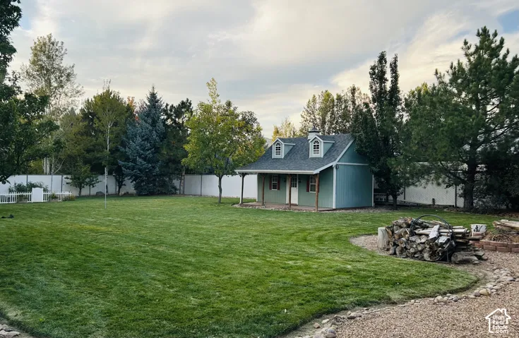 Expansive, fully fenced backyard with a sprawling lawn, charming outbuilding, fencedgarden and a fire pit area, surrounded by mature trees.