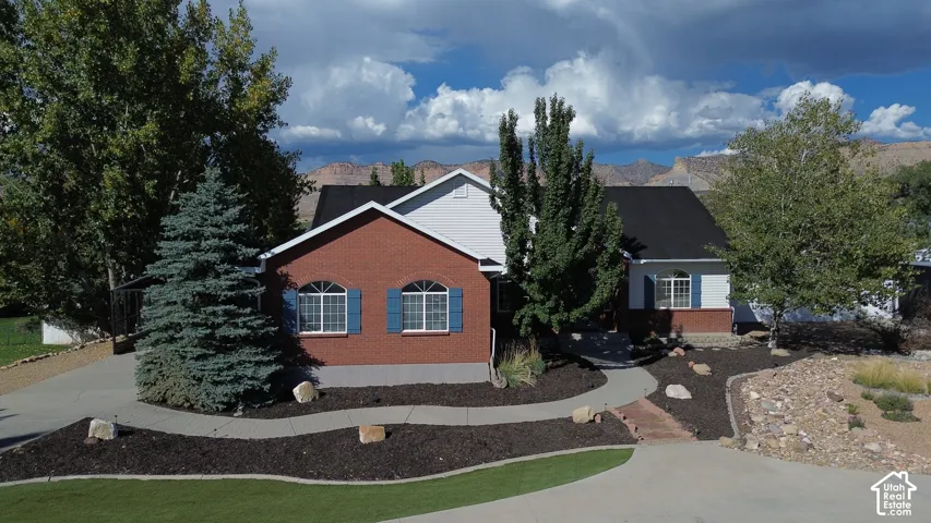 Brick and siding exterior featuring an arched window configuration, metal roofing, concrete driveway, and landscaped grounds with mature trees and mountain backdrop
