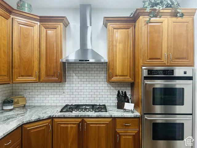 Chef-inspired cooking area with a five-burner gas cooktop, stainless chimney hood, doublewall ovens and subway tile backsplash.