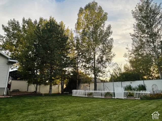 Fully fenced backyard with a white picket garden enclosure, mature shade trees and asprawling lawn.