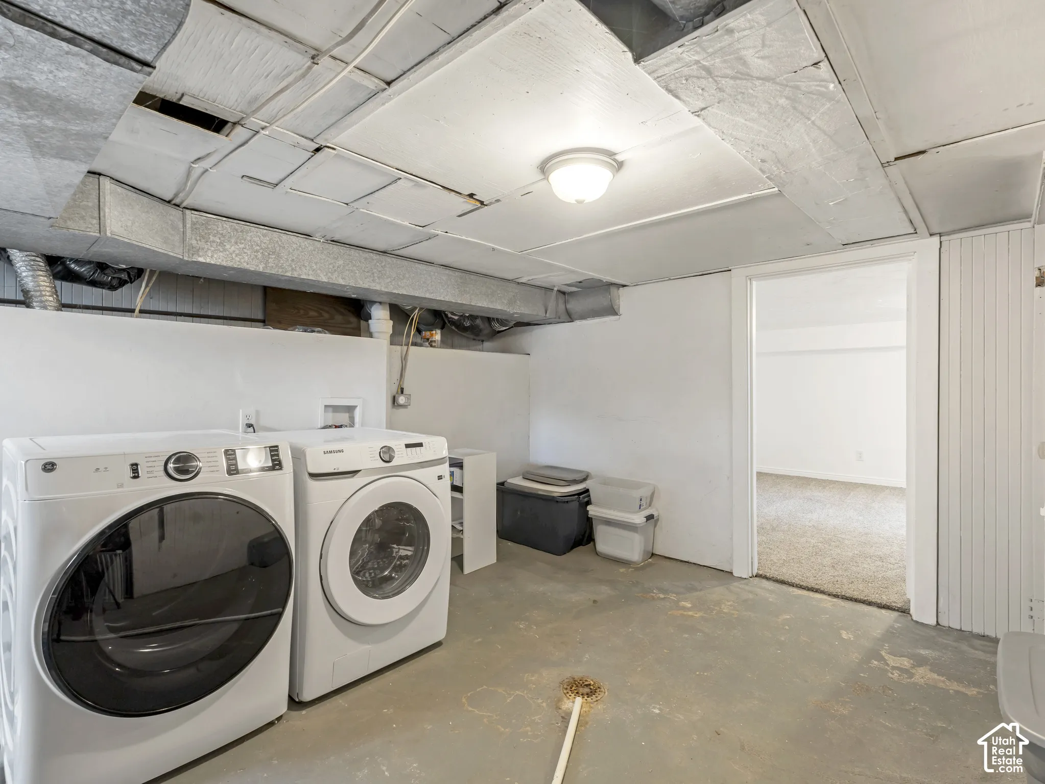 Laundry area with exposed ceiling utilities, concrete flooring, and white painted walls