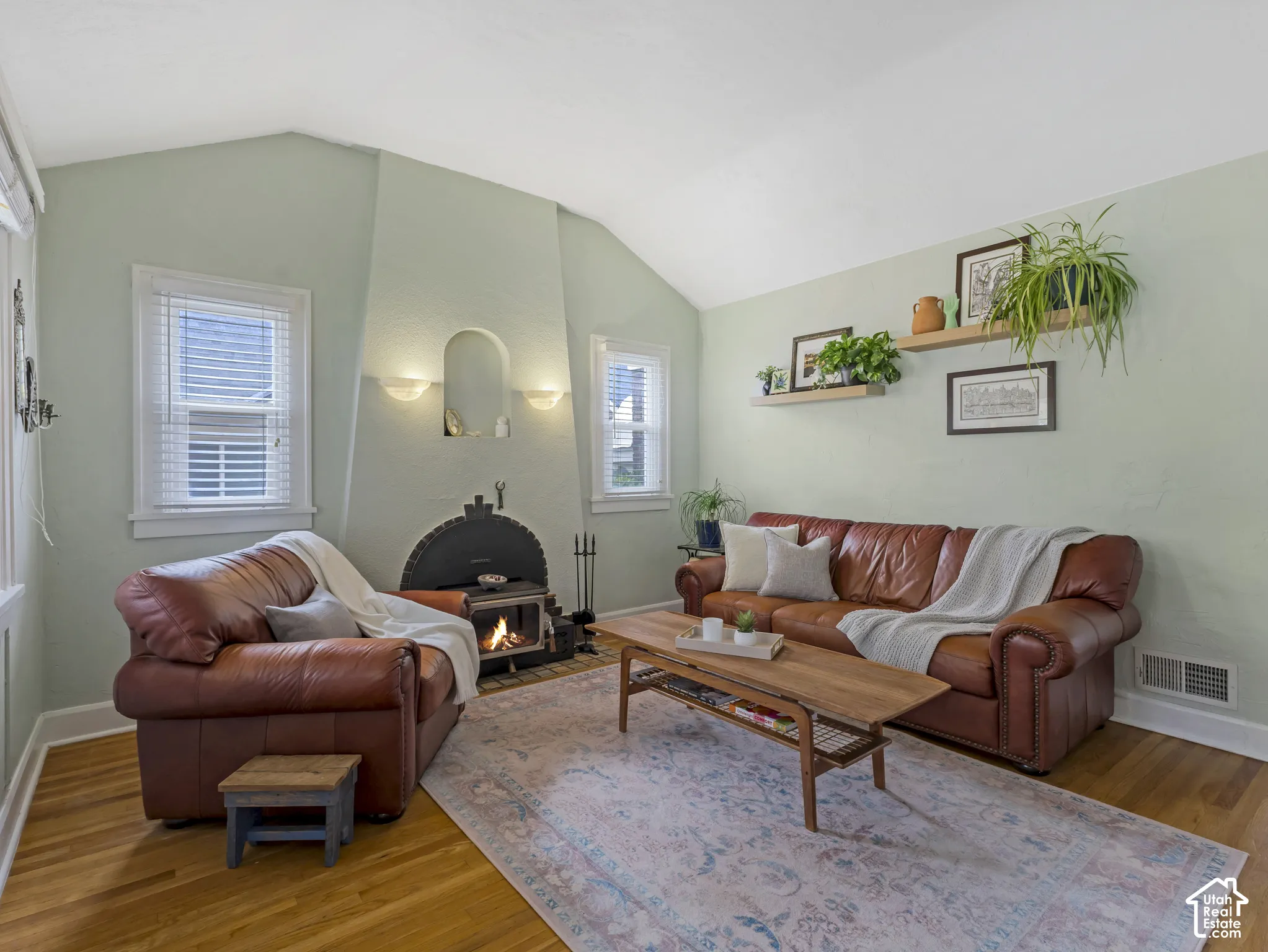 Vaulted ceiling, wood-finish flooring, wood-burning stove, arched fireplace alcove, and wall-mounted sconces