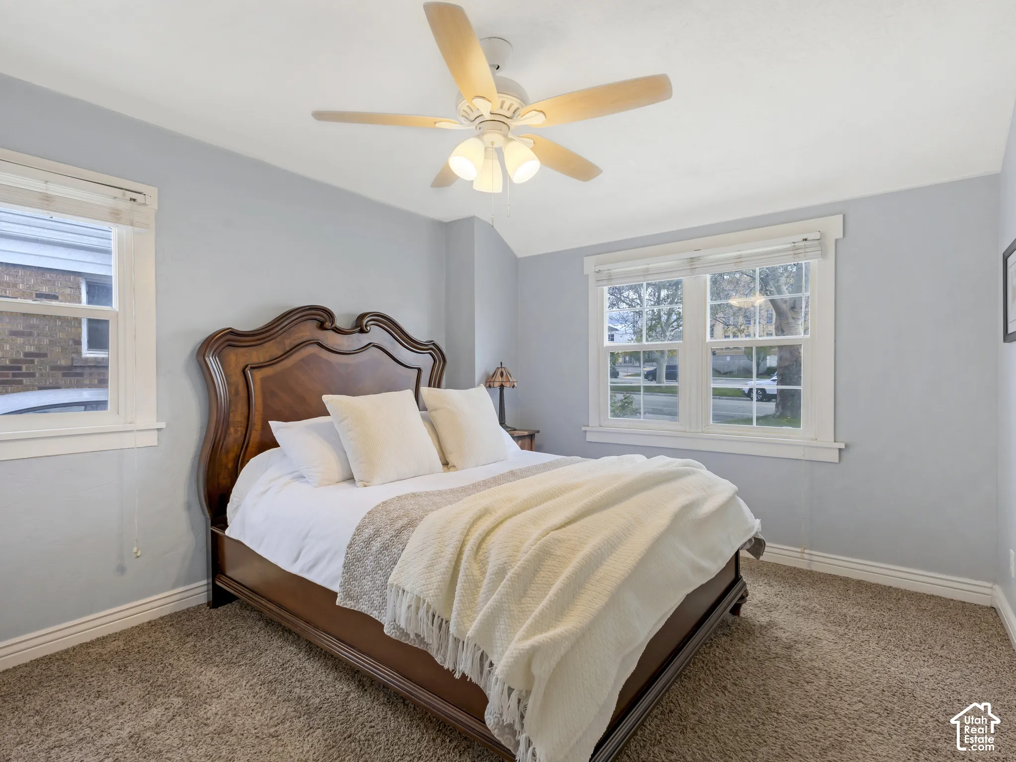 Neutral wall paint, ceiling fan with light kit, two windows with white trim, and carpet flooring
