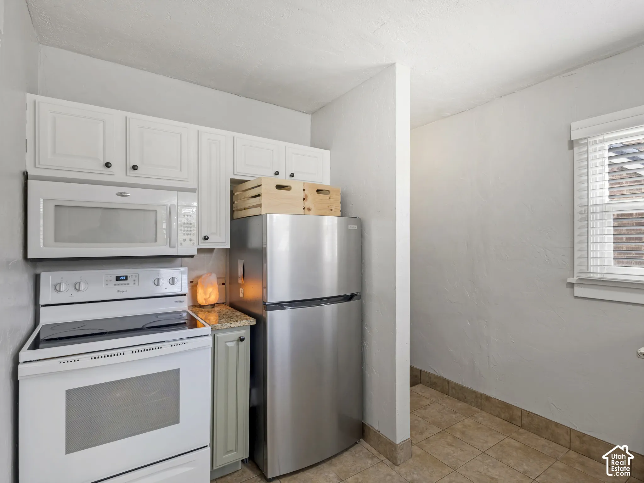 White cabinetry with dark hardware, stainless steel refrigerator, built-in microwave, white electric range, and tiled flooring