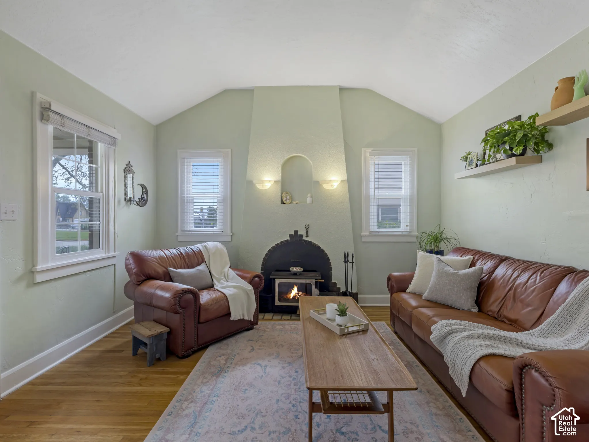 Hardwood flooring, arched fireplace with wood stove, recessed wall sconces, vaulted ceiling, and built-in shelving