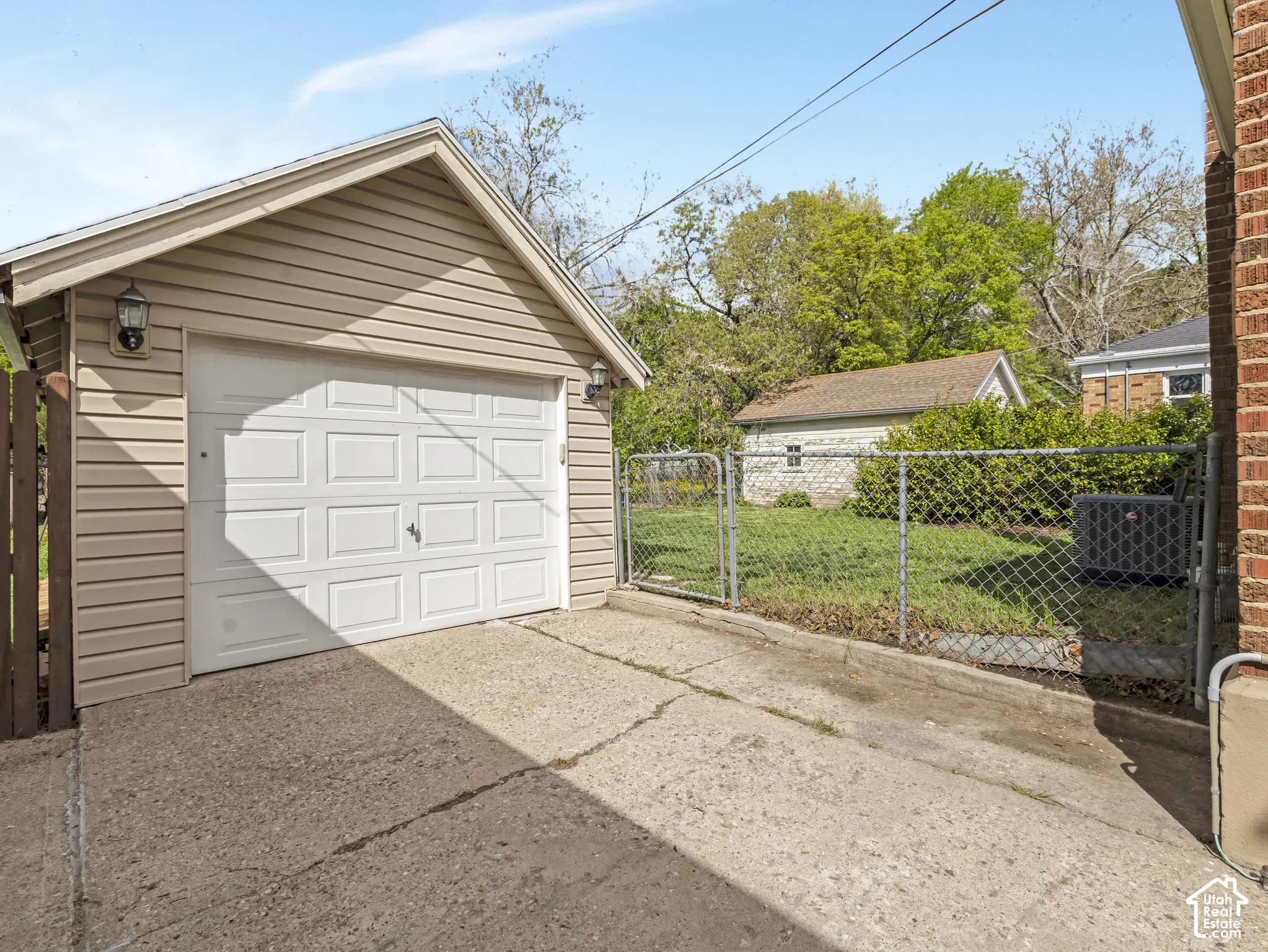 Detached garage with vinyl siding and a panel garage door, featuring exterior wall lanterns and a concrete driveway