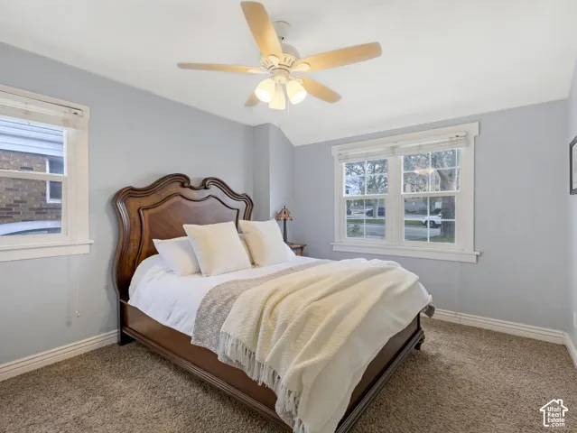 Neutral wall paint, ceiling fan with light kit, two windows with white trim, and carpet flooring