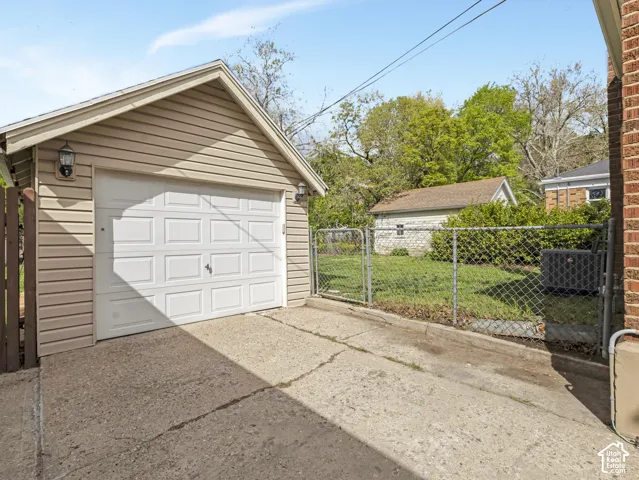 Detached garage with vinyl siding and a panel garage door, featuring exterior wall lanterns and a concrete driveway