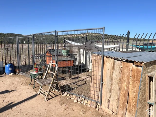 Enclosed animal run featuring metal fencing, a wood-sided structure with a corrugated metal roof, and an additional smaller structure within the enclosure