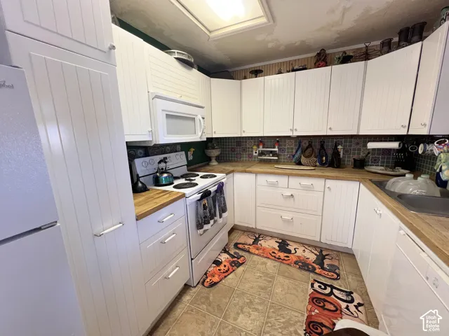 Kitchen featuring white beadboard cabinetry, wood-finish countertops, and a tile backsplash