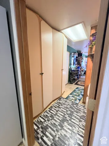 Recessed ceiling lighting illuminates a hallway featuring built-in cabinetry with light-toned doors, wood-finish flooring, and a door with a wood-finish frame