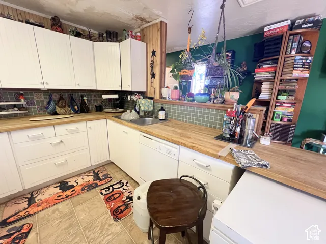 White cabinetry, light wood-finish countertops, tiled backsplash, built-in dishwasher, and a window with natural light