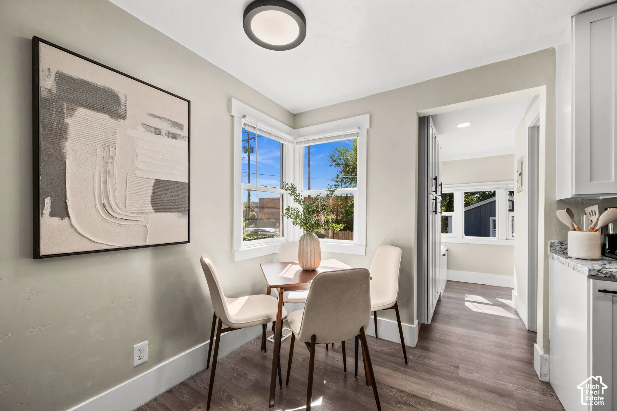 Recessed corner windows, wood-finish flooring, overhead flush-mount lighting, white kitchen cabinetry, and granite countertops