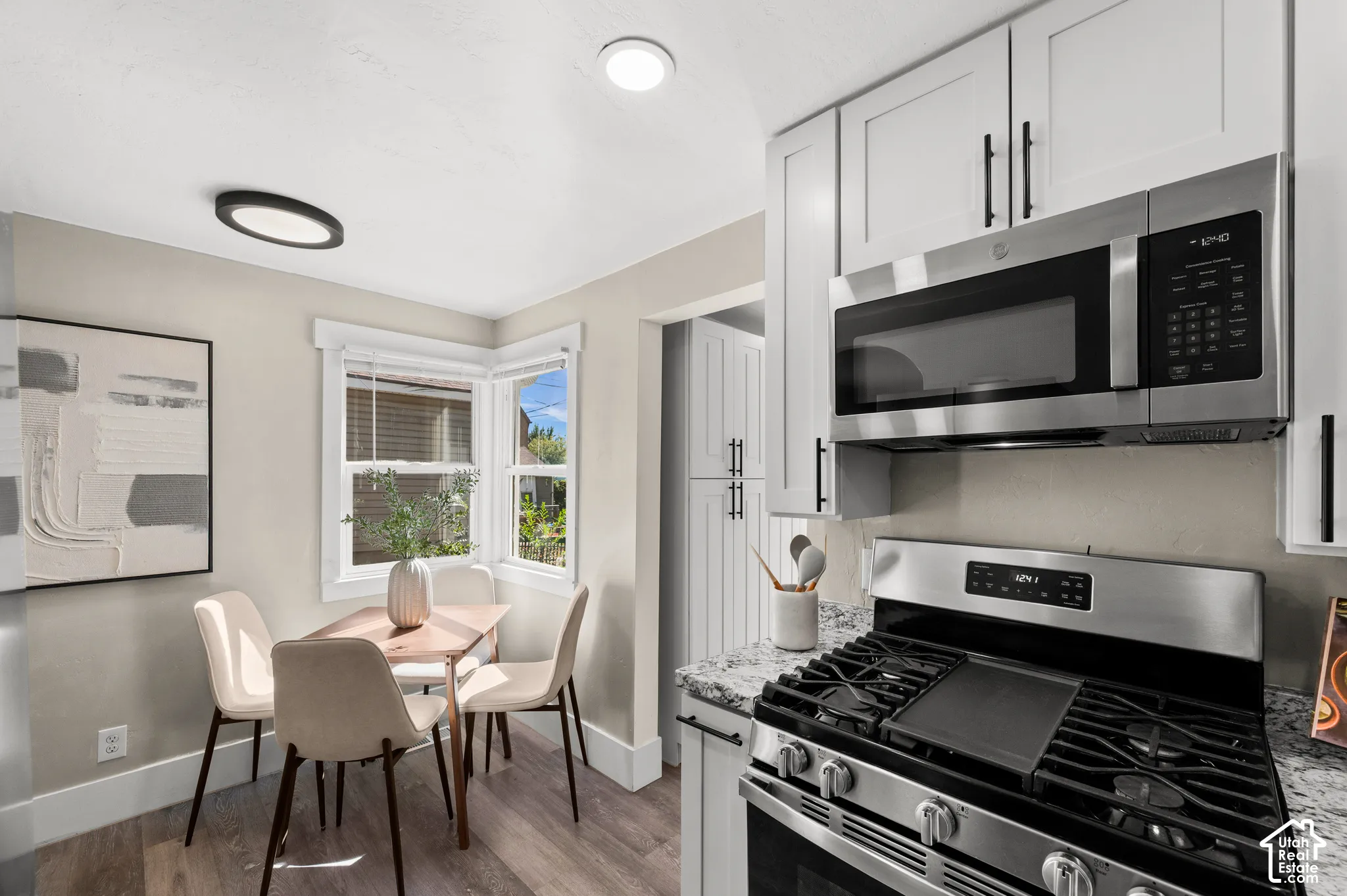 Updated kitchen featuring white shaker cabinetry, stainless steel appliances, speckled stone countertops, and wood-finish flooring
