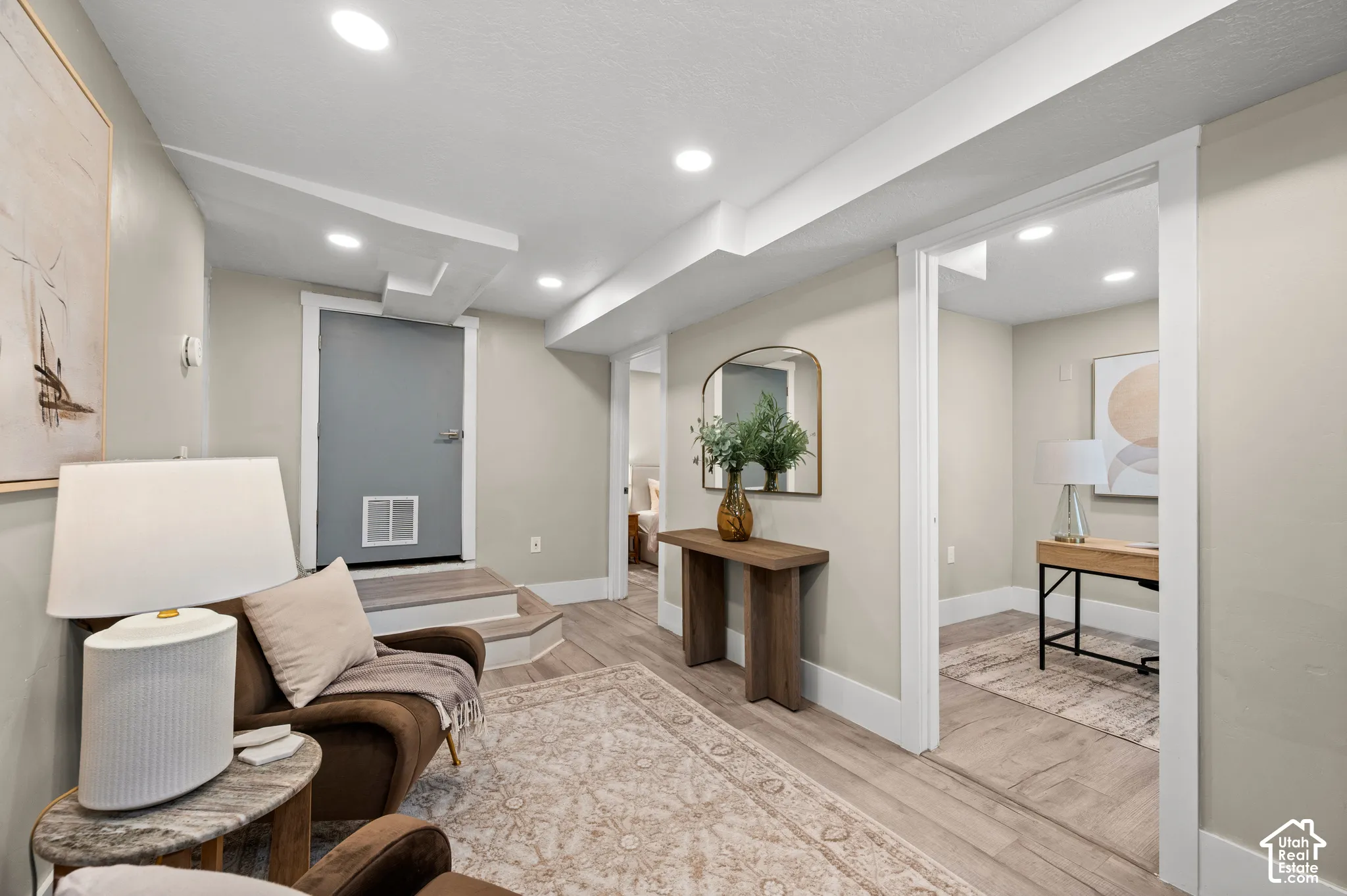 Recessed lighting, wood-finish flooring, light neutral wall tones, white trim work, and a grey door