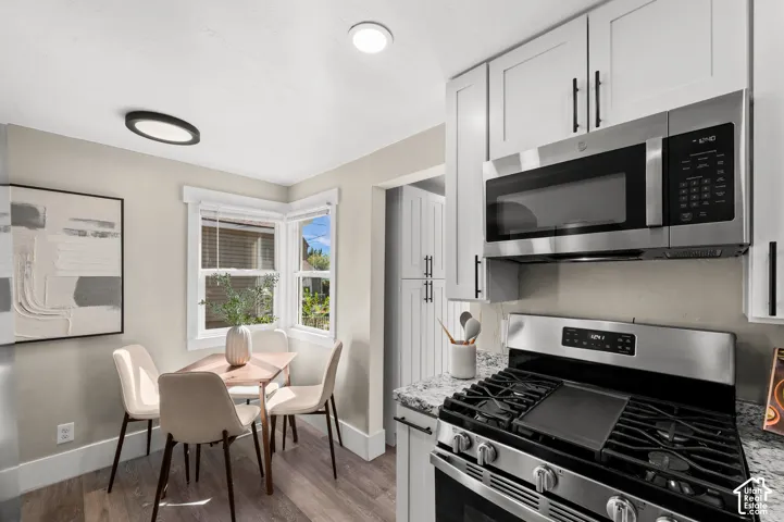 Updated kitchen featuring white shaker cabinetry, stainless steel appliances, speckled stone countertops, and wood-finish flooring