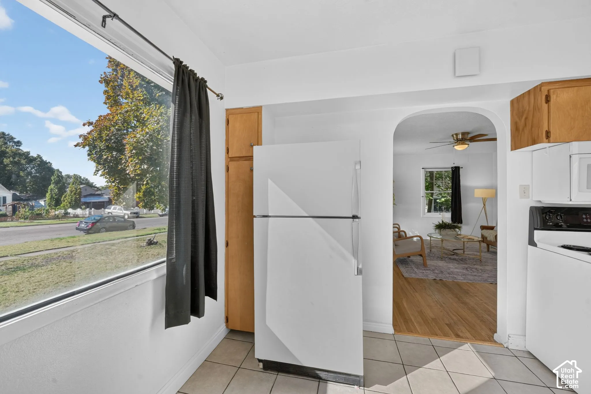 Kitchen featuring a white refrigerator, wood-finish cabinetry, built-in microwave, tile flooring, and an arched doorway