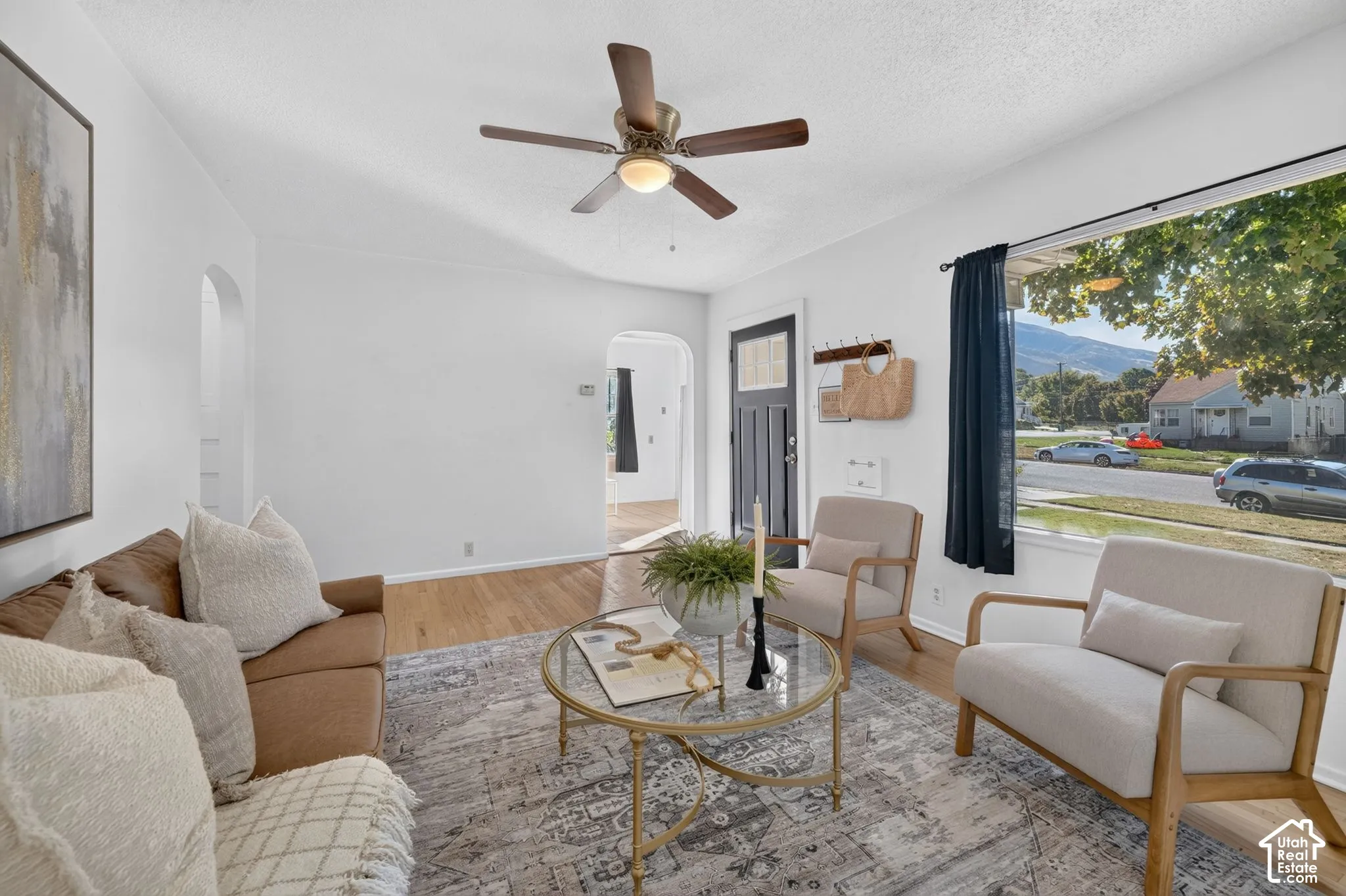 Bright living area featuring wood-finish flooring, a ceiling fan, and a large window with mountain scenery