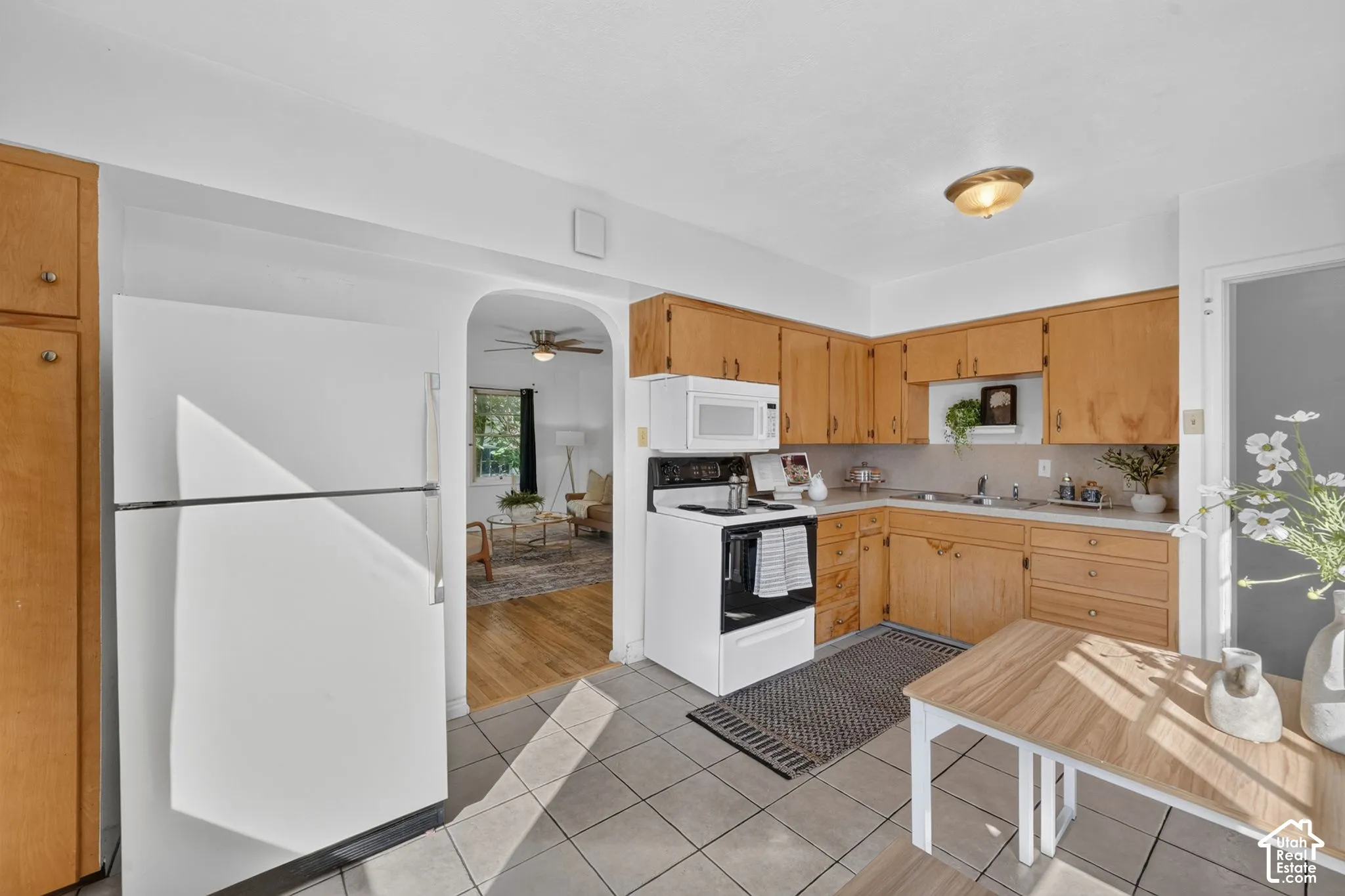 Kitchen featuring wood cabinetry, white appliances, tile flooring, and an arched doorway