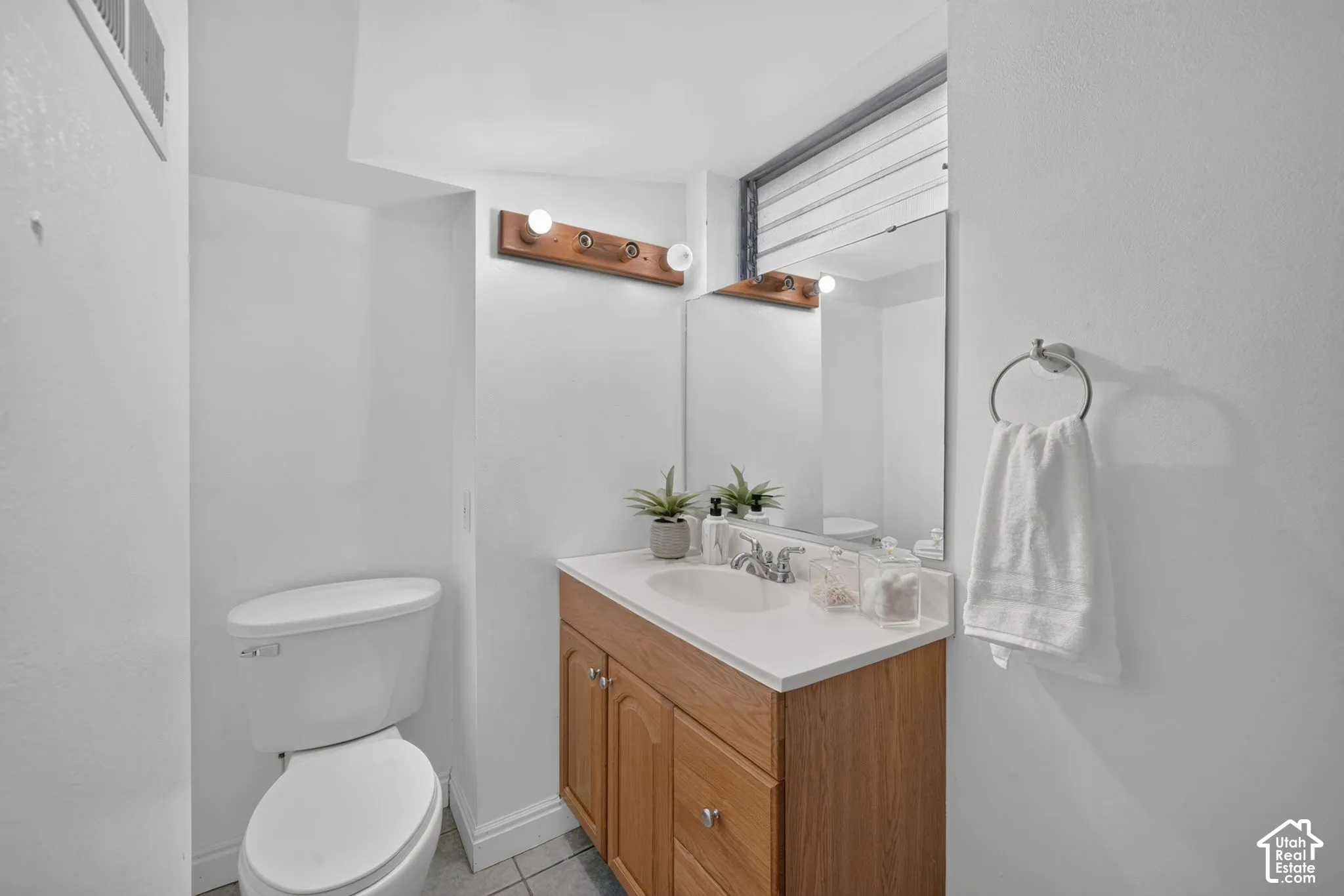 White vanity with a single basin, light wood-finish cabinetry, and a wall-mounted mirror