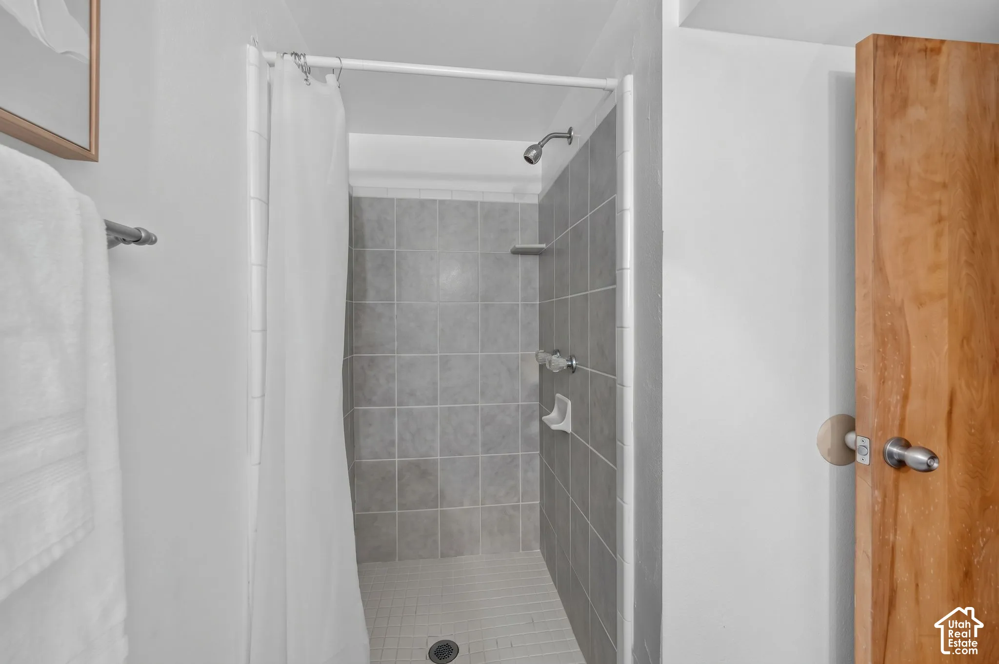 Shower featuring gray tiled walls, a white tiled floor, and a polished chrome showerhead