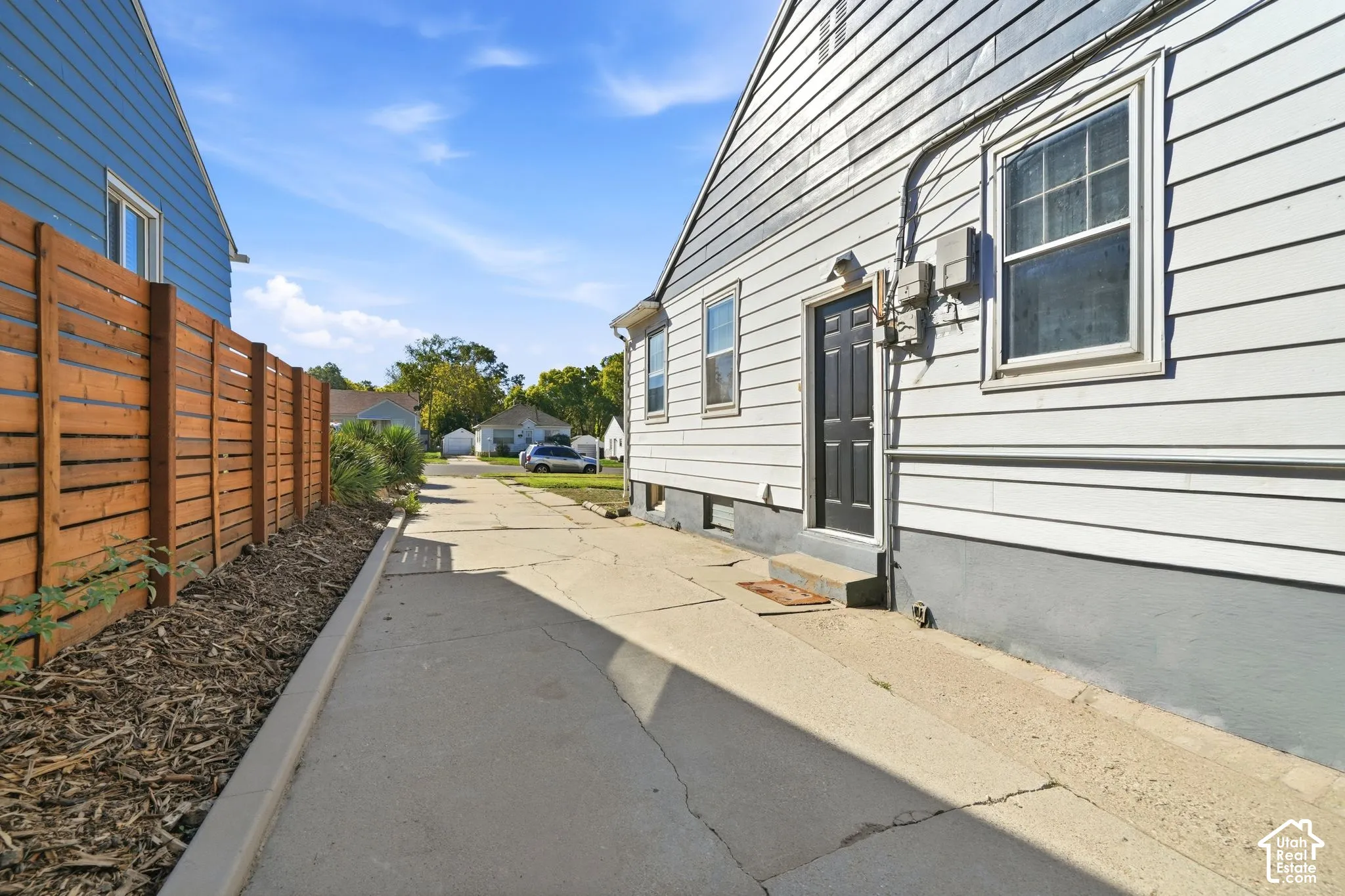 Siding exterior with a dark-paneled door, concrete drive, and a wood-slat privacy fence