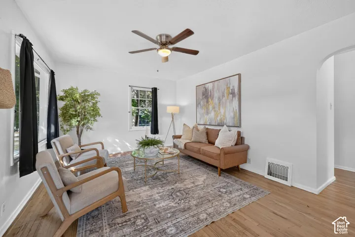 Hardwood flooring, white walls, multiple windows, ceiling fan, and an arched doorway