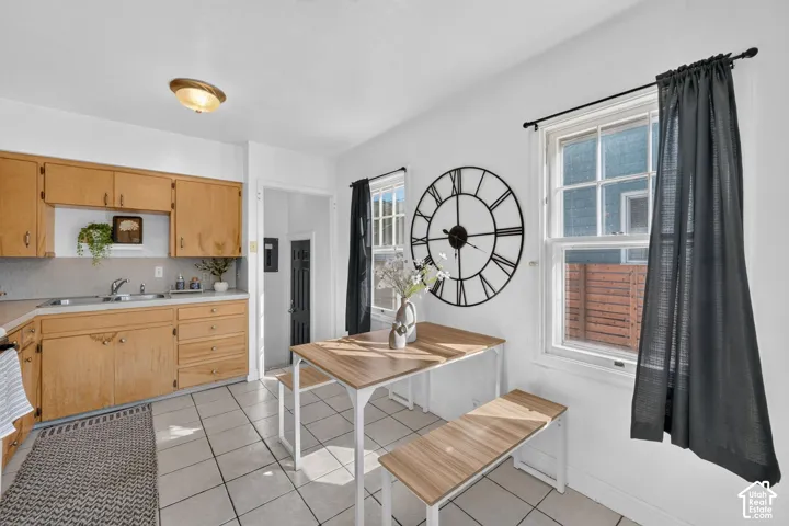 Kitchen space featuring light wood-finish cabinetry, solid surface countertops, a stainless steel sink, and white tile flooring
