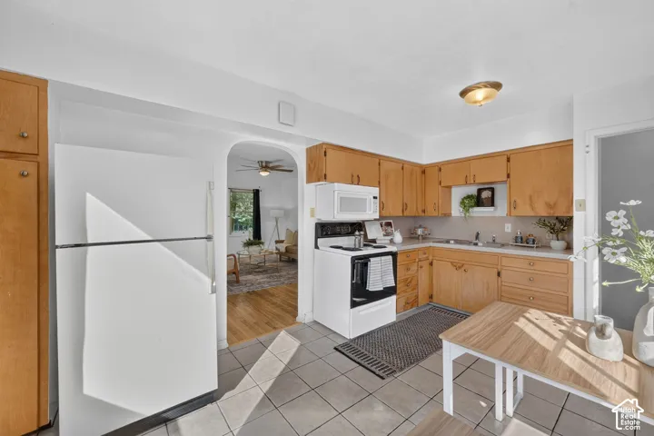 Kitchen featuring wood cabinetry, white appliances, tile flooring, and an arched doorway