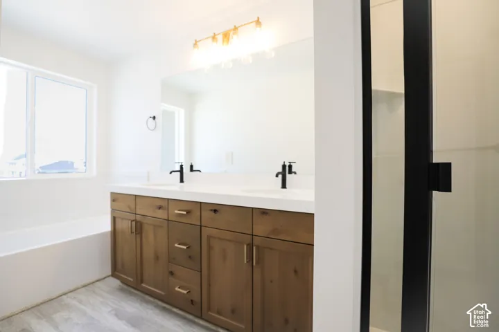 Primary bath with dual sinks, stained wood cabinets, quartz slab countertops, soaker tub and walk-in shower.