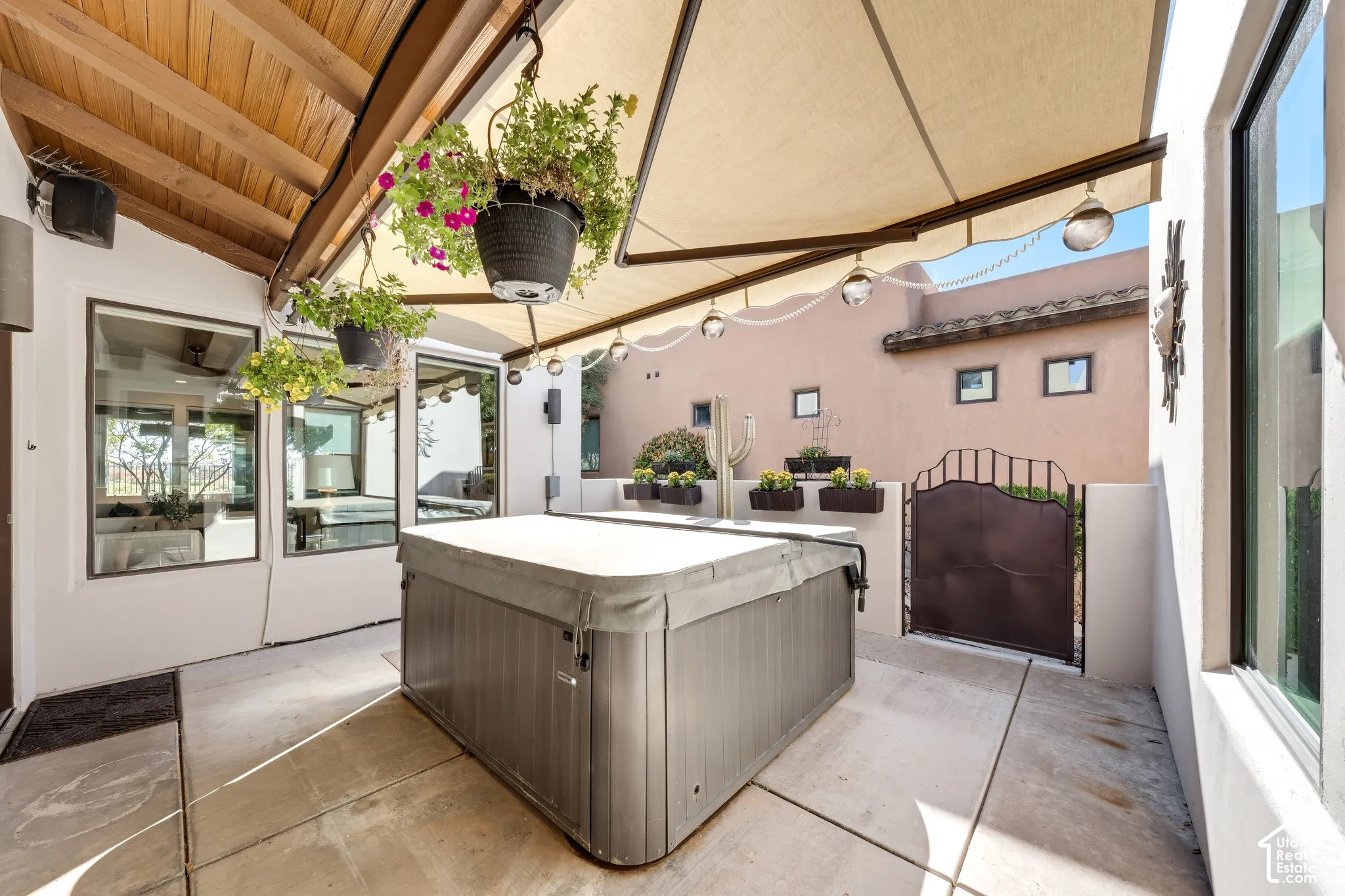 Covered patio with exposed wood beams, concrete flooring, built-in spa, and a wrought iron gate